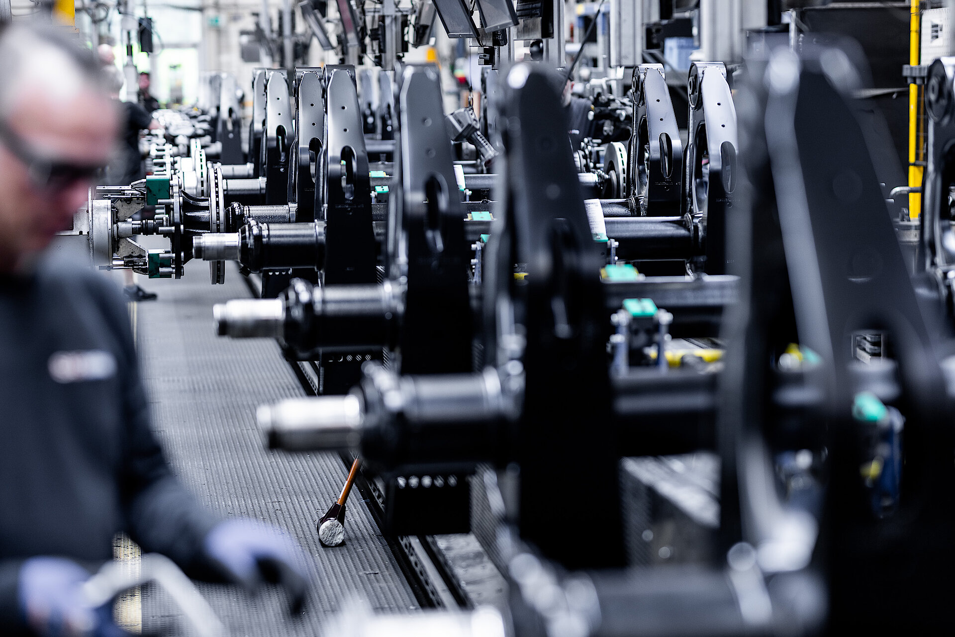 Production line with assembled axle components; an employee working blurred in the foreground.