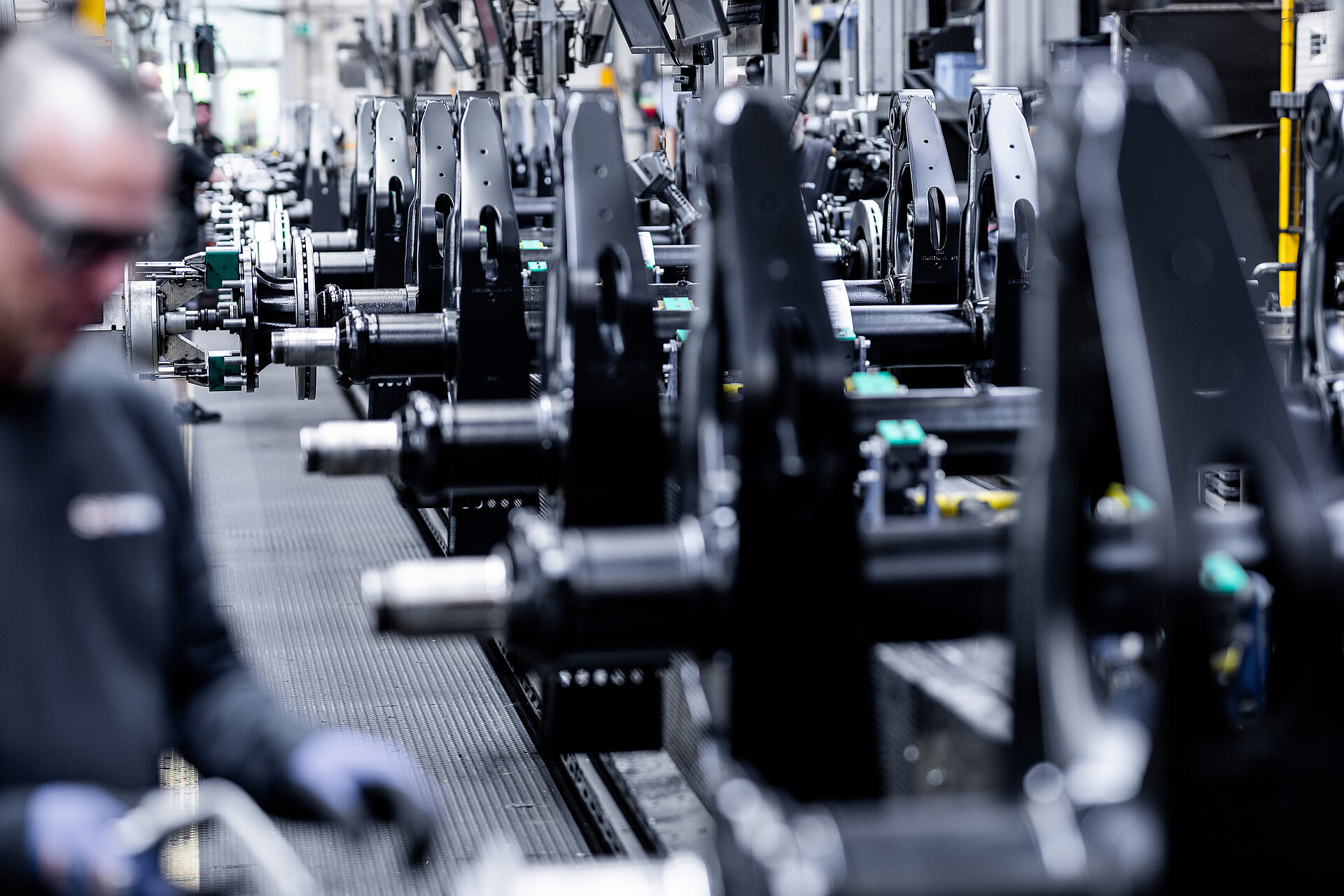 Production line with assembled axle components; an employee working blurred in the foreground.