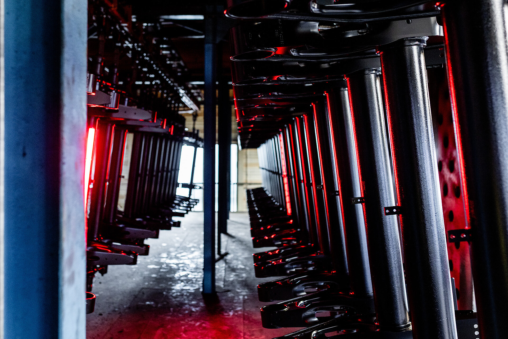 Axle components hang in a system and are illuminated with red light.