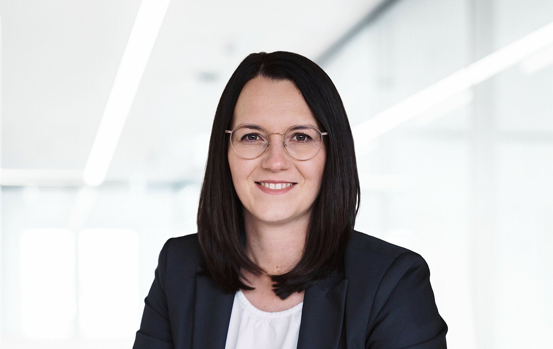 Woman in business attire smiling, background has soft focus office setting.