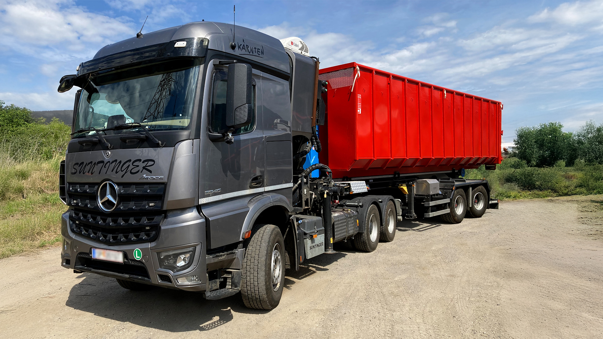 A dark grey truck with a red trailer is parked on a dirt road.